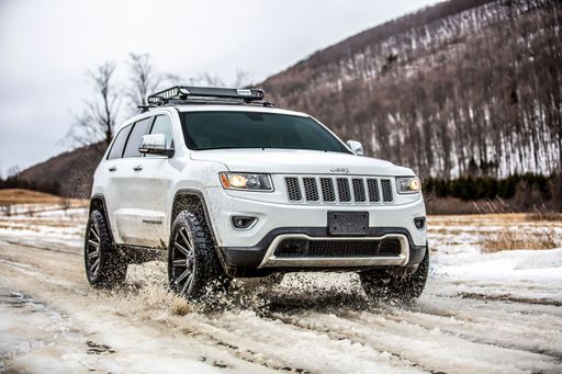 The white Jeep Grand Cherokee car driving through the snow.