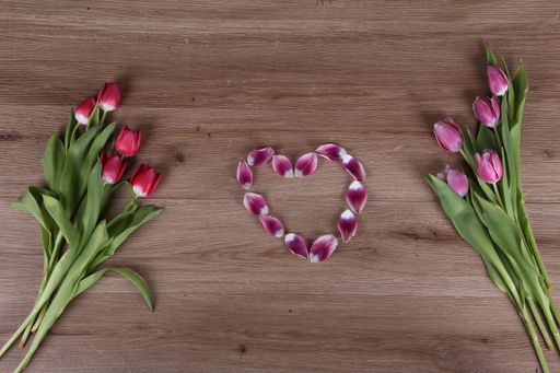 A top view of beautiful tulips and a heart on a wooden surface