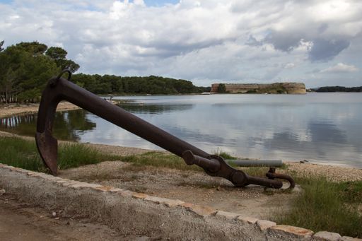 A closeup of an old rusty metal anchor with the lake and trees in the background
