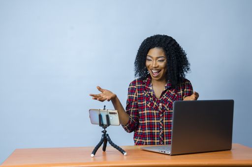 A closeup shot of a young Nigerian lady in a video call with laptop and phone on the desk