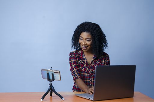 A closeup shot of a young Nigerian lady in a video call with laptop and phone on the desk