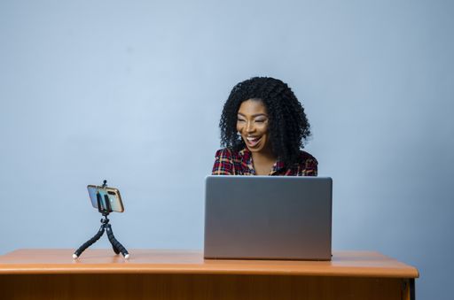 A closeup shot of a young Nigerian lady in a video call with laptop and phone on the desk