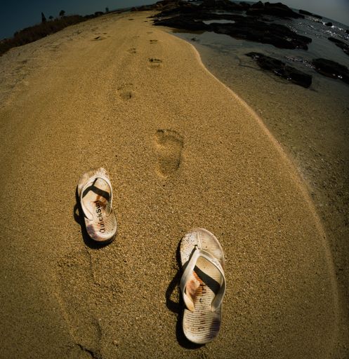 The high-angle view of flip-flops and feet track on the sand