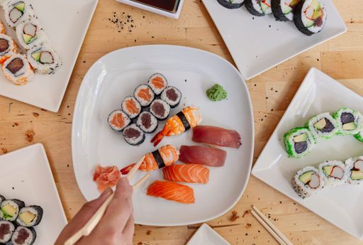 A top view of a person taking a piece of sushi with chopsticks on a wooden table