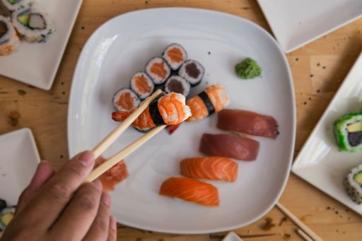 A top view of a person taking a piece of sushi with chopsticks on a wooden table