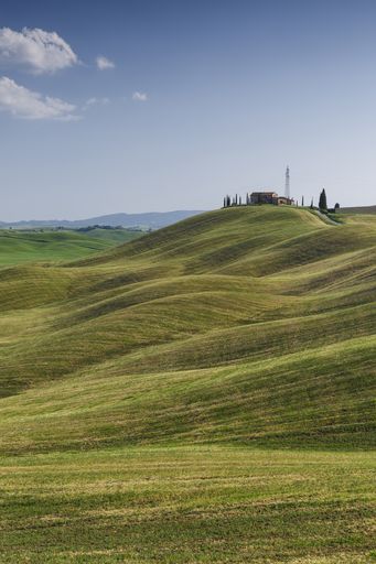 A vertical shot of the hills of Tuscany with a small lonely house visible in the background