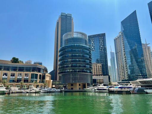 A low-angle shot of skyscrapers reflecting on the water with a blue sky in the background, Dubai, United Arab Emirates