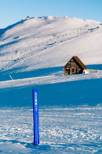 A vertical of a blue summit pole in a majestic ski resort with a wooden small house in the background