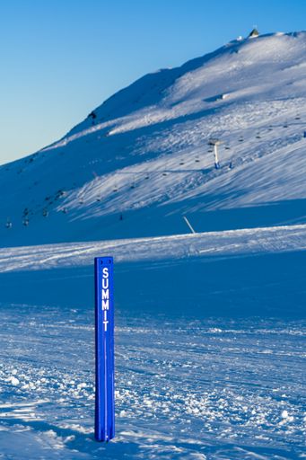 A vertical shot of a blue sign post that has been placed on the peak of a snowy mountain