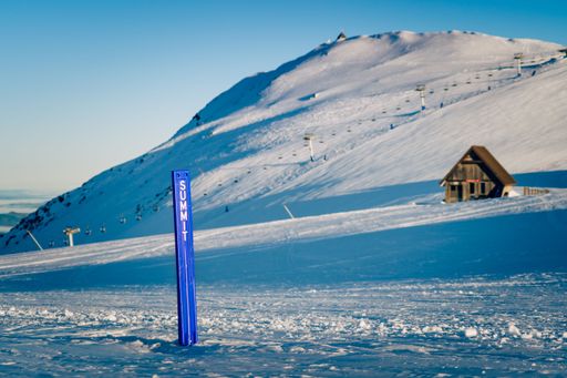 A scenic view of a blue sign post that has been placed on the peak of a snowy mountain
