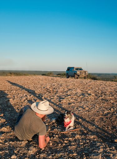 A vertical shot of a person controlling the drone using his phone sitting next to a cute dog