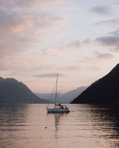 A vertical shot of the sailing boat on a lake with mountains in the background at sunset