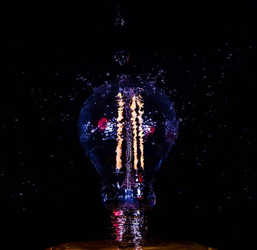 A vertical shot of water splashin on a lightbulb against a dark background