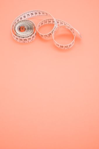 A vertical shot of a measuring tape isolated on coral background