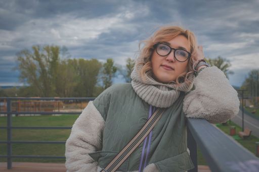 Young blonde woman in warm autumn clothes on river pier, leaning on parapet, and dreaming about something. Autumn mood.