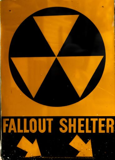 A vertical shot of a yellow "FALLOUT SHELTER" sign with arrows