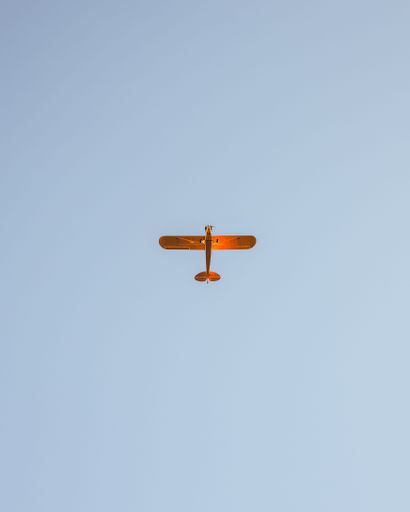 A low-angle shot of a crop plane flying against the blue sky