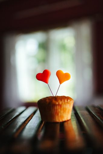 A vertical shot of a cupcake with colorful hearts on it