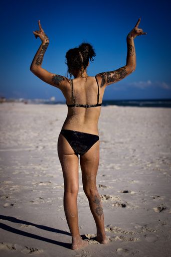 The vertical view of a brunette girl with tattoos on her arms standing at the beach from behind