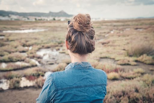 A back view of a female with a bun hairstyle sitting in a field