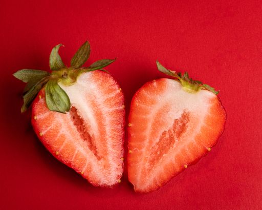 A closeup shot of a halved juicy strawberry on a red background