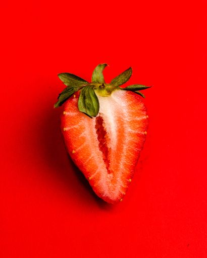 A vertical shot of a halved red strawberry on a red background