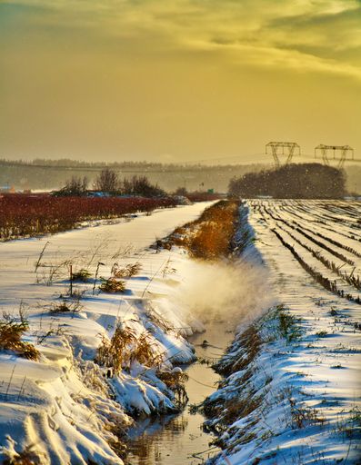A vertical top view of frozen stream in the middle of snow-covered field during sunset