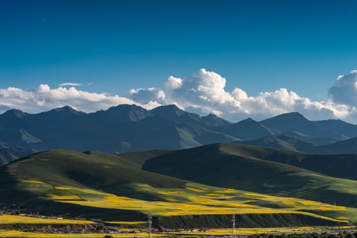 Several houses by beautiful mountains and grasslands in Xinjiang under a cloudy sky