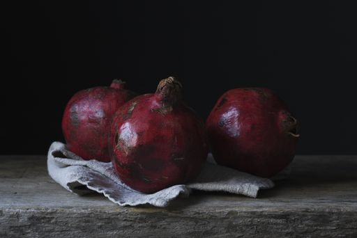 A still life photography shot of three gorgeous pomegranates on a wooden deck