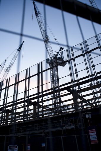 A vertical low angle shot of cranes in the process of construction of a building under the evening sky