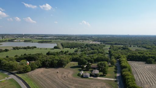 A drone shot of a backroad area near Royse City with lush trees and a lake under blue cloudy sky