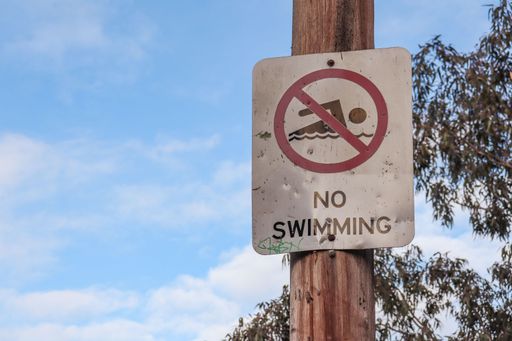 A "No Swimming" sign on a wooden pole with the sky and leaves in the background - concept of caution