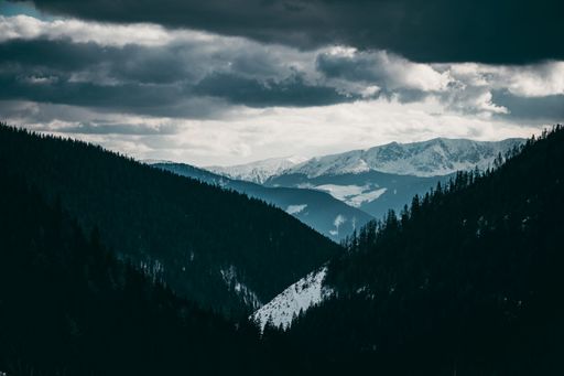 An aerial view of dense forests on snowcap Western Tatras mountain under dak dramatic cloudy sky