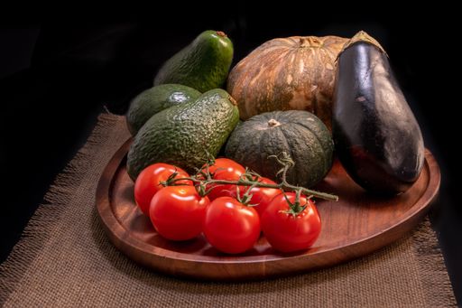A wooden board with vegetables and produce - tomatoes, avocados, eggplant and pumpkins