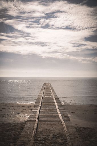 A vertical shot of a dock on the beach with a calm sea in the background on a sunny day - suitable for a wallpaper