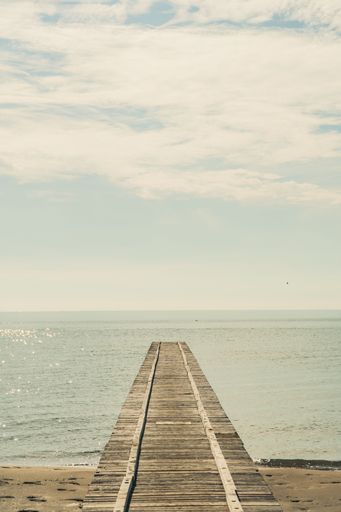 A vertical shot of a dock on the beach with a calm sea in the background on a sunny day - suitable for a wallpaper