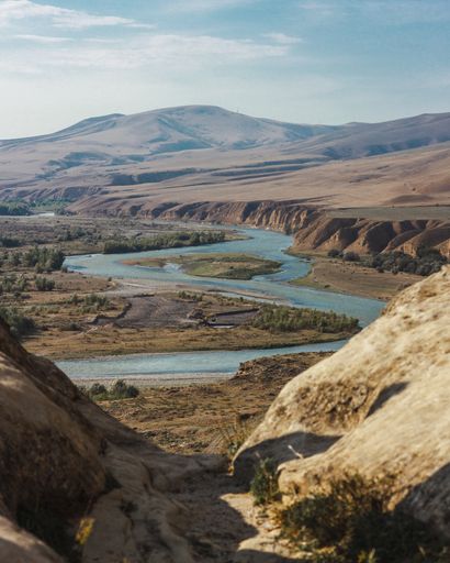 A high angle shot of a curvy river surrounded by high mountains under the cloudy sky