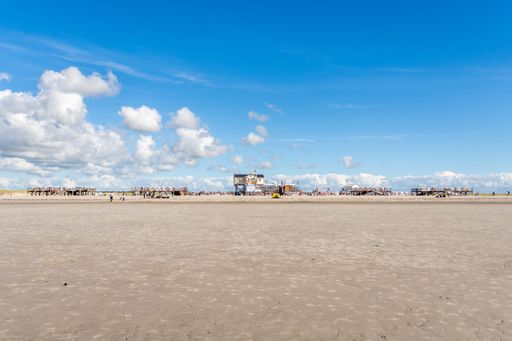 An old wooden jetty on the sandy beach of the North Sea in St. Peter-Ording against the blue sky