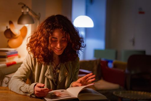 A young female with curly hair and happy facial expression reading a book in a room