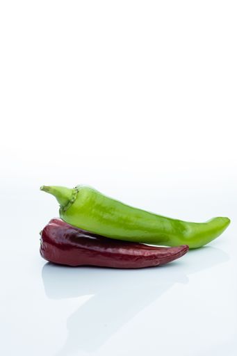 A green chili pepper and a dark red chili pepper isolated on a white background