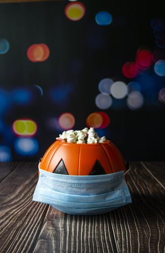 A vertical shot of a Halloween pumpkin with popcorn and a sanitary mask-concept of the new normal