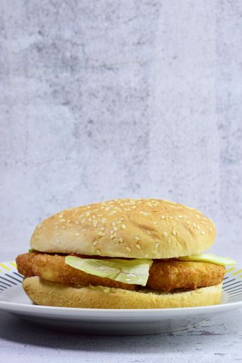 A vertical shot of a sandwich with chicken nuggets, lettuce and sesame buns on stone background