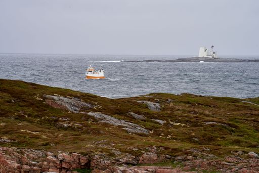 A small fishing boat cruising near the rocky coastline close to the Hestskjr lighthouse