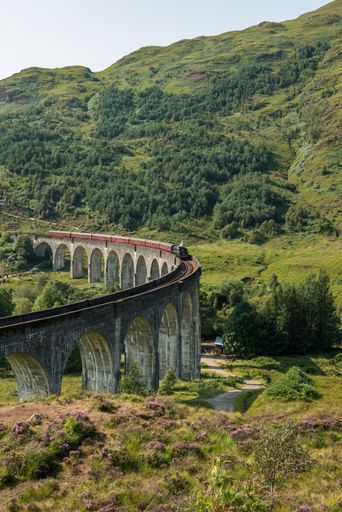 A vertical shot of the Glenfinnan Viaduct railway surrounded by green trees on a sunny day in spring