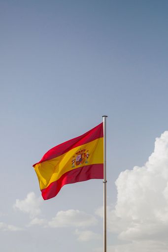 A vertical closeup of the flag of Spain against a cloudy blue sky