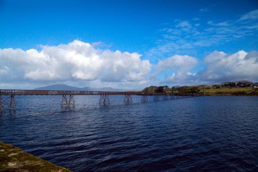 A narrow bridge stretching over a river under a blue sky