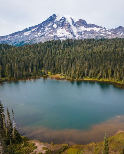 A vertical shot of a bright blue lake near the snowy Mount Rainier in Washington State