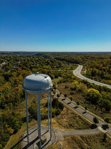 An aerial view of water tower on the hill overlooking roads between lush green forests