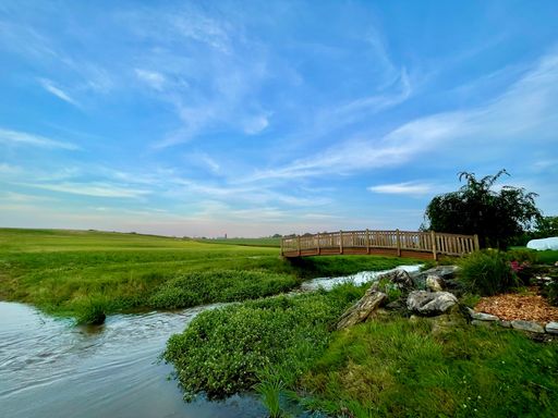 A scenic shot of a bridge over the stream in the green meadow under the blue sky
