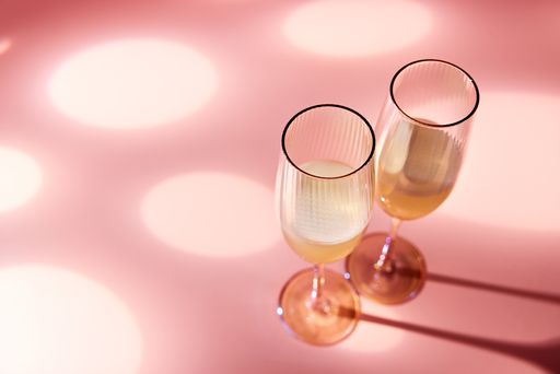 A sparkling champagne in crystal glasses served on a table on pink background in studio with sunlight